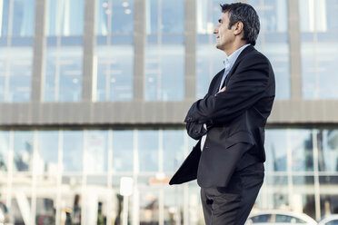 Businessman with arms crossed looking away outside office building - MASF05147