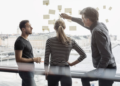 Businessman explaining adhesive notes to colleagues in office - MASF05171