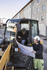 Construction workers discussing over blueprint at excavator - MASF05194