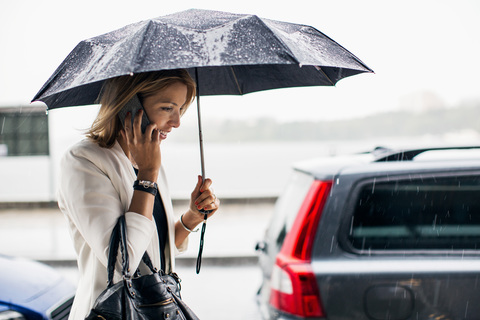 Geschäftsfrau, die während der Regenzeit in der Stadt mit einem Smartphone telefoniert, lizenzfreies Stockfoto