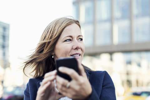 Geschäftsfrau schaut weg, während sie im Freien ein Mobiltelefon benutzt, lizenzfreies Stockfoto