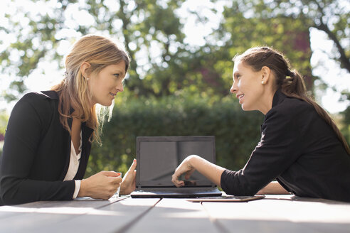Businesswoman discussing with female colleague through laptop at outdoor cafe - MASF05208