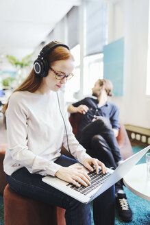 Geschäftsfrau mit Laptop in einem kreativen Büro mit einem Kollegen im Hintergrund - MASF05223