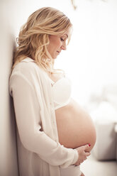 Side view of pregnant woman touching abdomen while leaning on wall at home - MASF05235