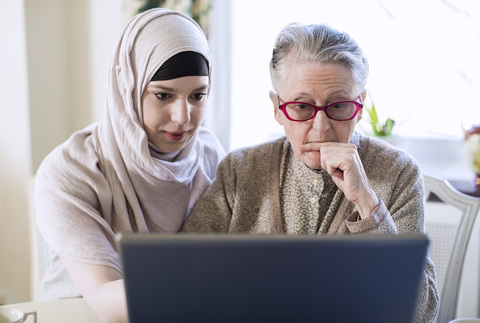 Ältere Frau und weibliche Betreuerin benutzen zu Hause einen Laptop, lizenzfreies Stockfoto