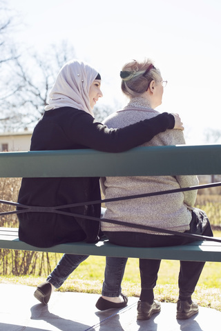 Rückansicht einer älteren Frau und einer häuslichen Pflegerin, die zusammen auf einer Parkbank sitzen, lizenzfreies Stockfoto