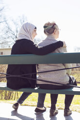 Rückansicht einer älteren Frau und einer häuslichen Pflegerin, die zusammen auf einer Parkbank sitzen - MASF05240