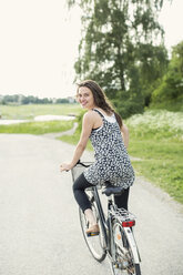 Rear view portrait of young woman cycling on country road - MASF05257