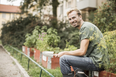 Side view portrait of happy man with shovel sitting in garden - MASF05265