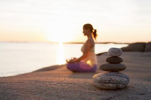 Side view of woman sitting in lotus position on lakeshore with focus on stack of stones - MASF05276
