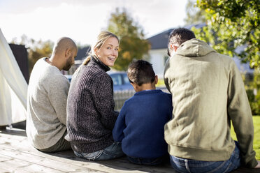 Rear view portrait of smiling woman sitting with family at yard - MASF05277