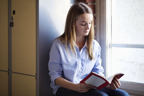 Schulmädchen, das am Fenster in der Umkleidekabine ein Buch liest - MASF05282