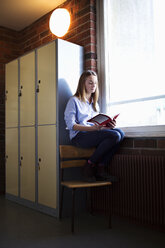 Schoolgirl studying by window in locker room - MASF05283