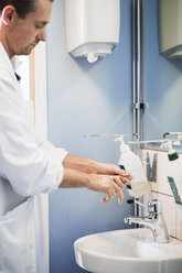 Side view of male doctor washing hands in hospital bathroom - MASF05289