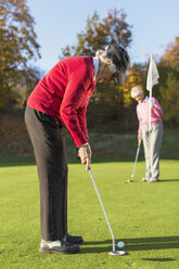 Side view of senior woman putting while friend holding flag on golf course - MASF05296