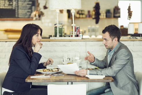 Seitenansicht eines Geschäftsmannes mit einer weiblichen Kollegin, die an einem Restauranttisch Papierkram besprechen - MASF05300