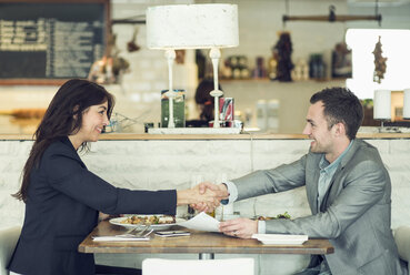 Side view of businessman and businesswoman shaking hands at restaurant table - MASF05301