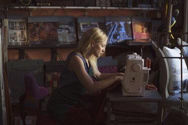 Seitenansicht einer jungen Modedesignerin mit einer Nähmaschine im Atelier - MASF05312