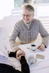 Young female home caregiver consoling senior woman while having coffee on porch - MASF05317