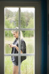 View of woman using mobile phone through closed door - MASF05324