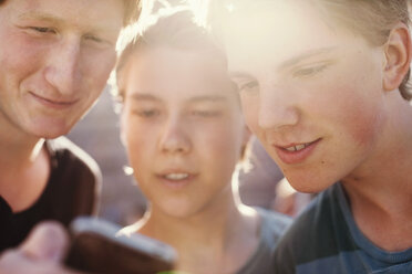 Junge männliche Freunde lesen gemeinsam eine Textnachricht auf einem Mobiltelefon im Freien - MASF05325
