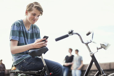 Junger Mann, der auf dem Fahrrad sitzend auf der Straße ein Mobiltelefon benutzt - MASF05329