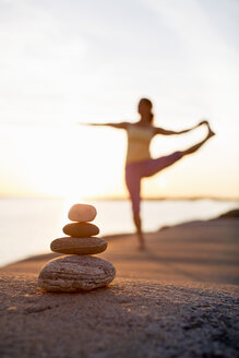 Woman practices yoga on lakeshore with focus on pile of stones - MASF05345