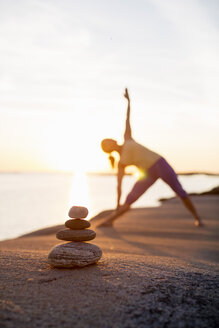 Woman practices yoga on lakeshore with focus on stack of stones - MASF05346