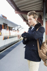 Junger Geschäftsmann schaut auf dem Bahnhof auf die Uhr - MASF05354