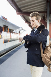 Young businessman looking at watch on railroad station - MASF05354