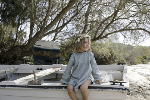 Lächelndes kleines Mädchen mit Blumen auf einem Boot am Strand sitzend, lizenzfreies Stockfoto