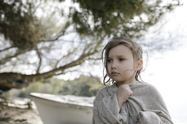 Portrait of sad little girl wrapped in oversized cardigan standing on the beach - KMKF00188