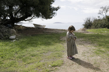 Little girl wrapped in oversized cardigan standing on a meadow - KMKF00189