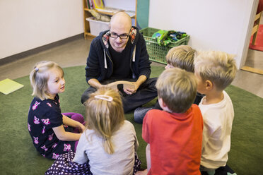 Lehrerin und Schüler sitzen auf einem Teppich im Kindergarten - MASF05411