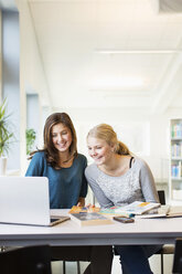 Lächelnde Teenager-Mädchen mit Laptop am Tisch in der Schulbibliothek - MASF05416