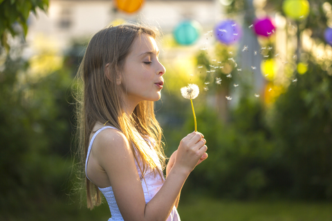 Mädchen bläst Pusteblume im Garten, lizenzfreies Stockfoto
