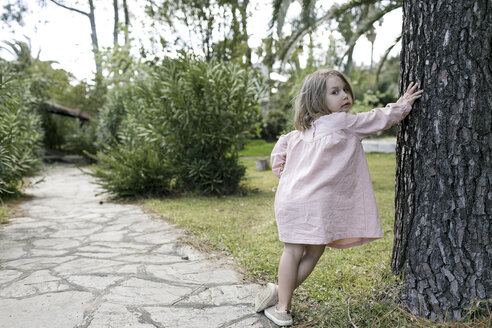 Porträt eines kleinen Mädchens, das sich im Garten an einen Baumstamm lehnt - KMKF00194