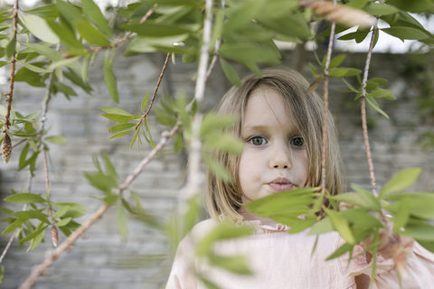 Porträt eines kleinen Mädchens zwischen Zweigen in einem Garten, lizenzfreies Stockfoto