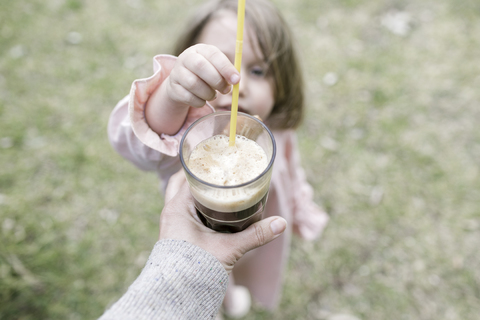 Kleines Mädchen, das einen Strohhalm in ein Glas mit Kaffee steckt, lizenzfreies Stockfoto