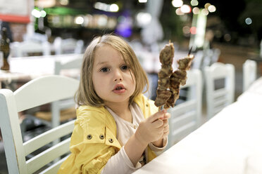 Griechenland, Porträt eines kleinen Mädchens, das in einem Restaurant mit zwei Souvlaki-Fleischspießen sitzt - KMKF00205