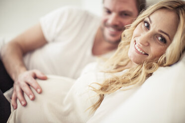 Porträt einer glücklichen schwangeren Frau mit einem im Bett liegenden Mann - MASF05421
