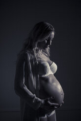 Pregnant woman standing in dark at home - MASF05424