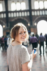 Porträt einer glücklichen Frau mit Mobiltelefon auf einem Bahnhof - MASF05431