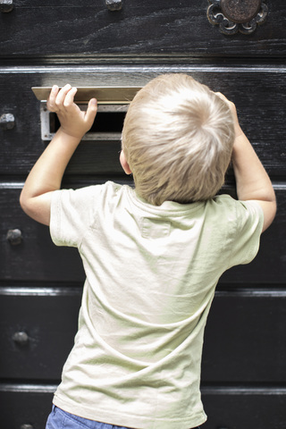 Rückansicht eines kleinen Jungen, der durch den Briefschlitz der Tür schaut, lizenzfreies Stockfoto