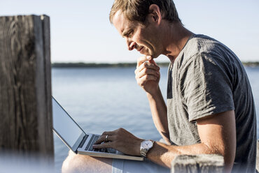 Profilaufnahme eines reifen Mannes mit Laptop auf einem Pier - MASF05435