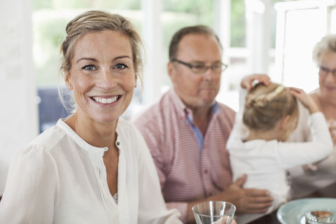 Porträt einer lächelnden Frau, die mit ihrer Familie am Esstisch sitzt, lizenzfreies Stockfoto