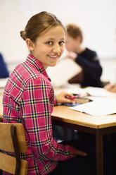 Porträt einer glücklichen Schülerin am Schreibtisch im Klassenzimmer - MASF05454