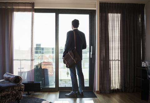 Rückansicht eines Geschäftsmannes, der durch das Fenster eines Hotelzimmers schaut, lizenzfreies Stockfoto
