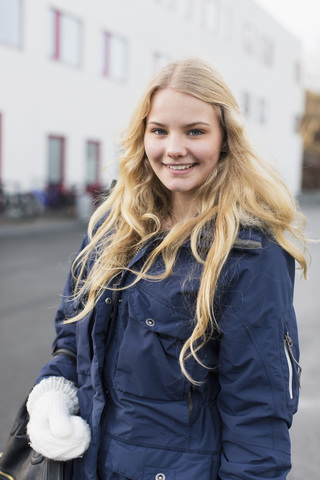 Porträt eines glücklichen Teenagers mit Wintermantel auf dem Schulgelände, lizenzfreies Stockfoto