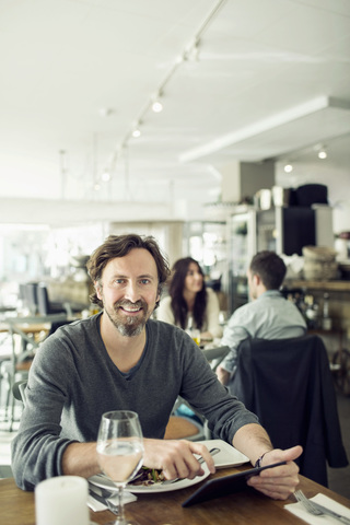 Porträt eines reifen Geschäftsmannes, der ein digitales Tablet im Restaurant benutzt, lizenzfreies Stockfoto